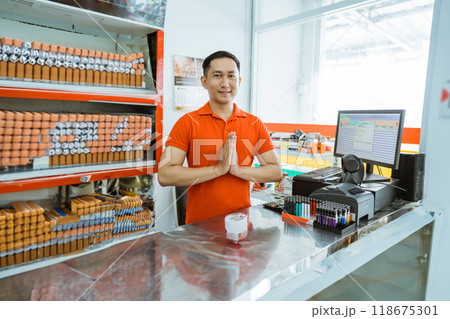 male store clerk smiles at the camera with a greeting gesture 118675301