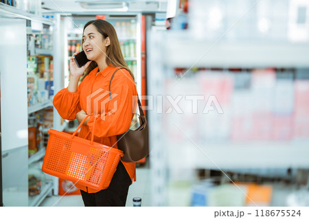 young Asian woman carrying bag and shopping cart while calling 118675524