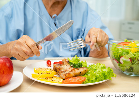 Asian elderly woman patient eating salmon stake and vegetable salad for healthy food in hospital. 118680124
