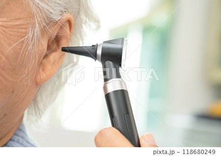 Audiologist or ENT doctor use otoscope checking ear of asian senior woman patient treating hearing loss problem. 118680249