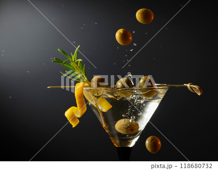 Classic dry martini cocktail with green olives, lemon peel, and rosemary on a black background. 118680732