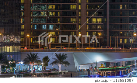 Yachts and boats with tourists staying near shoping mall and passing under a bridge in Dubai Marina district night timelapse. 118681097