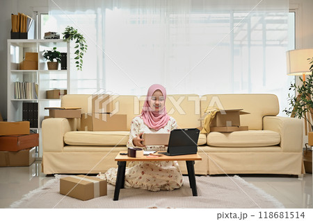 Smiling Asian muslim woman using digital tablet for receiving online purchase order. Small business concept 118681514
