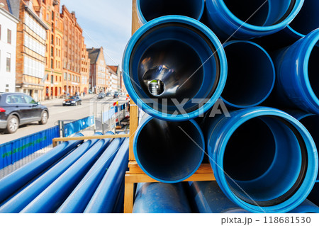 Close-up blue PVC plumbing pipes stacked wooden pallets replacement at german city street infrastructure construction site. Town development building industrial background 118681530
