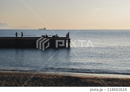 Silhouettes of male fishermen fishing on pier in the sea in the evening Silhouettes of male fishermen fishing on pier in the sea in the evening 118681628