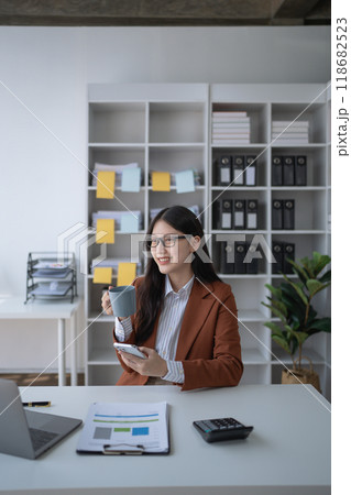 A businesswoman takes a break from her financial tasks, relaxing with a cup of coffee to recharge before continuing her work. 118682523