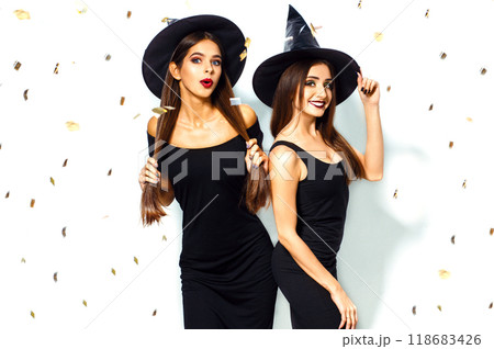 nice portrait of two beautiful young woman in black witch halloween costumes on party over white background. nice portrait of two beautiful young woman in black witch halloween costumes on party over white background. 118683426