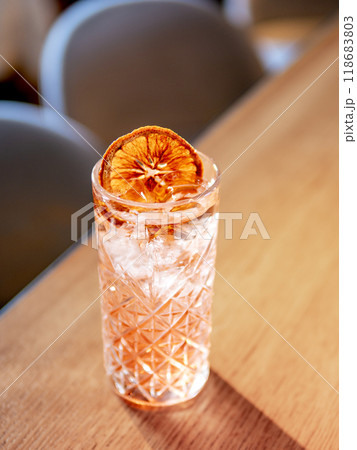 Transparent pink alcohol cocktail with ice, vodka and gin-tonic on bar counter in restaurant interior. Alcohol cocktail decorated orange slice. Cold alcoholic cocktail in bar or nightclub. Copy space 118683803