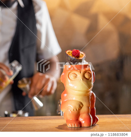 Tiki Drink Cocktail. One tropical tiki cocktail on bar counter. Tiki cocktail in monkey mug decorated fig and raspberry on bar in night club 118683804