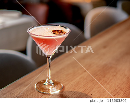 Red cocktail in martini glass on bar counter in restaurant interior. Gin alcohol cocktail decorated egg white and dry lichee fruit slice. Pink cold alcoholic cocktail in bar or nightclub background 118683805