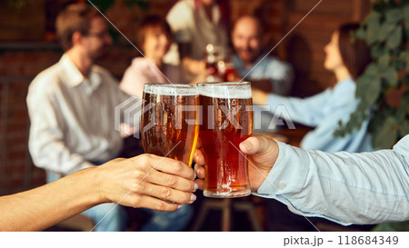 Close-up cheers, while blur of friends behind celebrate with raised glasses. Scene set for a great game day with friends and beer. Close-up cheers, while blur of friends behind celebrate with raised glasses. Scene set for a great game day with friends and beer. 118684349