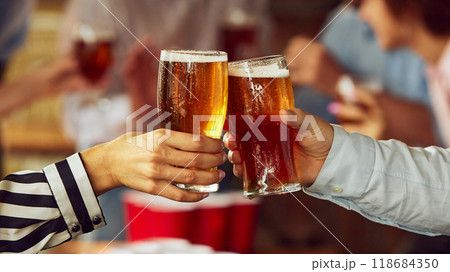 Couple of fans clink their glasses, surrounded by warm, blurred scene of sports lovers and friends. Excitement and tension of game build up. Couple of fans clink their glasses, surrounded by warm, blurred scene of sports lovers and friends. Excitement and tension of game build up. 118684350