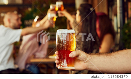 Glasses of beer raised high, sport fans cheer in celebration. Blurry crowd in background mirrors their joy, sharing moment. Glasses of beer raised high, sport fans cheer in celebration. Blurry crowd in background mirrors their joy, sharing moment. 118684379