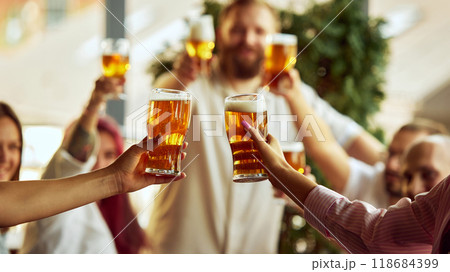 Sport fans in vibrant scarves toast with beer, their excitement visible even in blurred background as they celebrate together. Sport fans in vibrant scarves toast with beer, their excitement visible even in blurred background as they celebrate together. 118684399