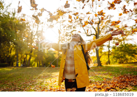A smiling tourist in a bright coat walks through an autumn park in sunny weather. Travel concept. 118685019