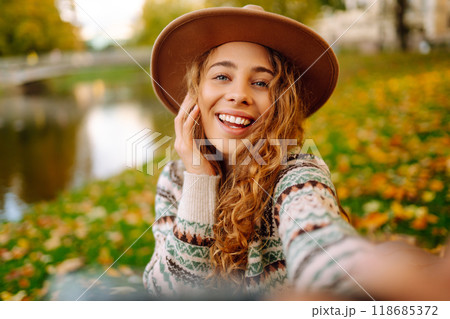 Happy woman in stylish sweater and hat outdoors in autumn park on plaid. Woman enjoys autumn nature. 118685372