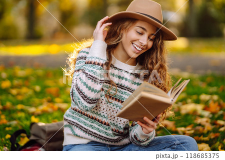 Beautiful curly woman in hat on mat with book in autumn park. Relaxation, solitude with nature. 118685375