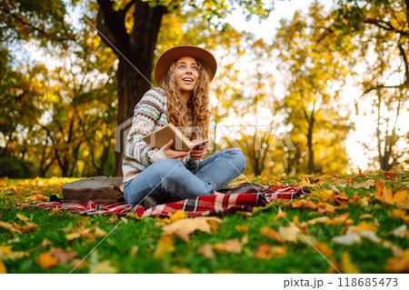 Beautiful curly woman in hat on mat with book in autumn park. Relaxation, solitude with nature. Beautiful curly woman in hat on mat with book in autumn park. Relaxation, solitude with nature. 118685473