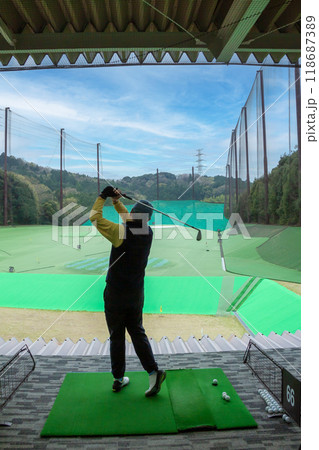 山の中のゴルフ練習場でスイングをするシニア男性 118687389