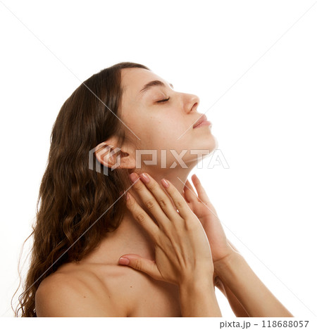 Young, attractive woman softly massaging her neck, illustrating relaxation and wellness against white studio background. 118688057