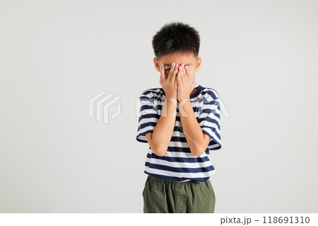 Asian portrait young kid boy in depressed bad mood covering face with hands and peering out with one eye between fingers studio shot isolated on white background, primary child surprised and shocked Asian portrait young kid boy in depressed bad mood covering face with hands and peering out with one eye between fingers studio shot isolated on white background, primary child surprised and shocked 118691310