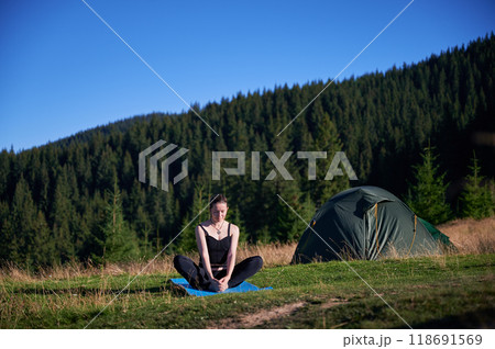 Woman practicing yoga and meditating outdoors in the mountains in a serene, natural setting. Female performing yoga pose on mat. 118691569