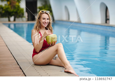 Smiling Woman Relaxing by Poolside Holding Coconut Drink 118692747