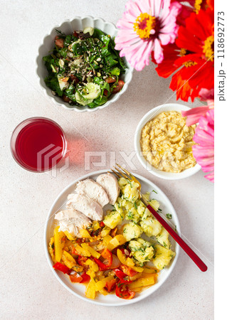 A balanced meal of boiled potatoes with baked vegetables and chicken breast, paired with a fresh tomato and cucumber salad topped with seeds, and a refreshing raspberry compote 118692773