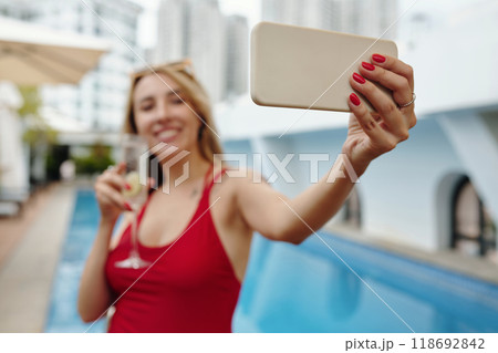 Taking Selfie by Swimming Pool Holding Cocktail Glass 118692842