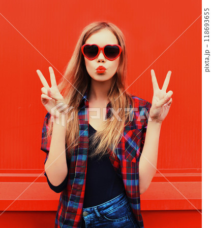 Portrait pretty young woman in red sunglasses shape of heart blowing lips making air kiss outdoors 118693655