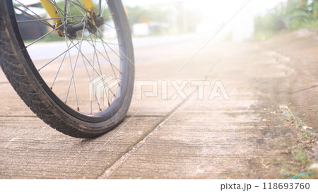 Wheel of a bicycle is flat parking on concrete sidewalk beside a road, need to be repaired, the moment of stillness and an unexpected pause in a journey. Wheel of a bicycle is flat parking on concrete sidewalk beside a road, need to be repaired, the moment of stillness and an unexpected pause in a journey. 118693760