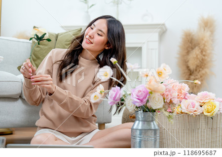Pretty Asian woman sit on the floor and hold the flower during do flower arrangement in living room of her house with relax time. 118695687