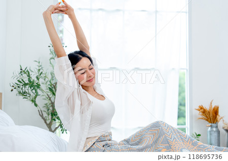 Beautiful Asian woman wake up and stretch oneself on bed in the morning with happiness. 118695736