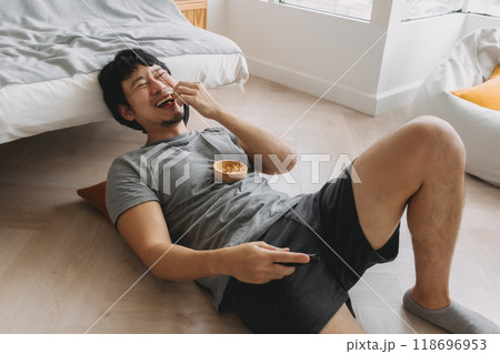 Man lying on the floor eating snack and laughing at the TV on weekends. Man lying on the floor eating snack and laughing at the TV on weekends. 118696953