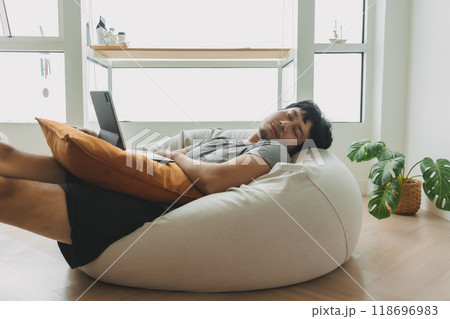 Man sleep over the laptop lying on the bean bag sofa in living room. 118696983