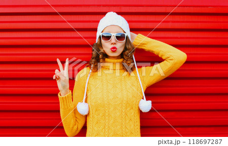 Fashion woman blowing red lips wearing colorful knitted yellow sweater hat over red background 118697287