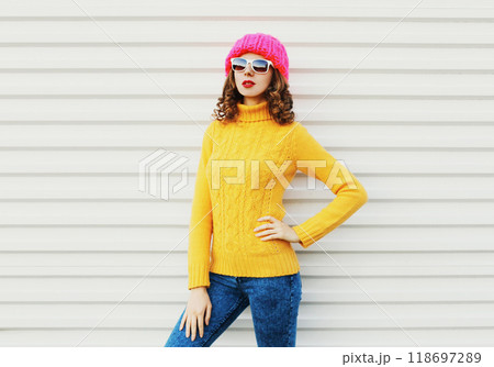 Fashion young woman model wearing a knitted pink hat, yellow colorful sweater over white background 118697289