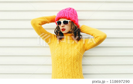 Fashion young woman wearing a knitted pink hat, yellow colorful sweater over white background 118697290