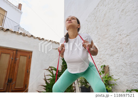 Woman exercising outdoors with a resistance band focusing on strength and fitness in a serene backyard setting 118697521