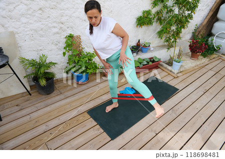 Woman exercising with resistance band on wooden deck surrounded by plants in a serene outdoor setting 118698481