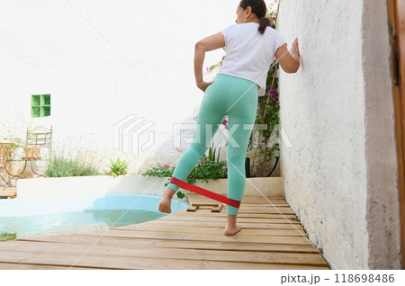 Woman exercising with a resistance band outdoors by the pool on a sunny day 118698486