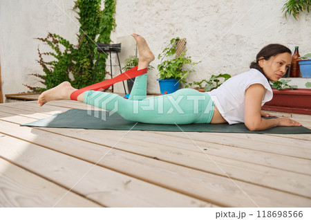 Woman practicing outdoor fitness with resistance band on yoga mat in peaceful garden setting 118698566