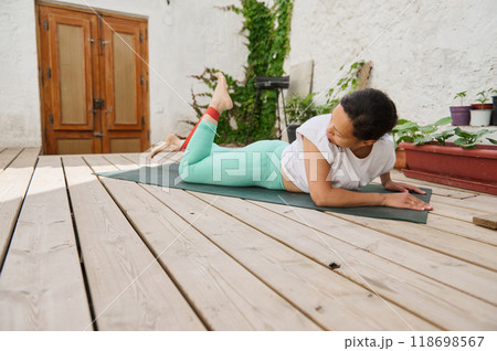 Woman practicing yoga outdoors on wooden deck in peaceful setting, wearing casual workout attire and engaging in relaxation and fitness Woman practicing yoga outdoors on wooden deck in peaceful setting, wearing casual workout attire and engaging in relaxation and fitness 118698567