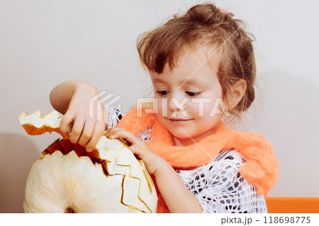 Little girl in Halloween costume curving pumpkin for holiday decoration. Little girl in Halloween costume curving pumpkin for holiday decoration. 118698775