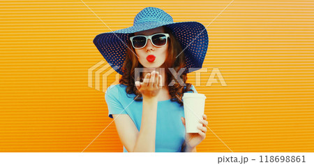 Portrait of beautiful young woman blowing kiss in summer straw hat, blue dress on orange background 118698861