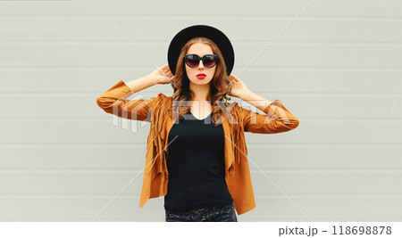 Fashion pretty woman model wearing a black hat, sunglasses, jacket posing on grey background Fashion pretty woman model wearing a black hat, sunglasses, jacket posing on grey background 118698878
