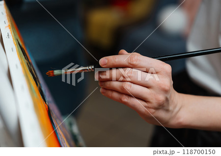 A close-up of an artists hand painting on canvas with a brush in a studio 118700150