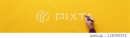 Male hand about to write on blank yellow background Male hand about to write on blank yellow background 118700353