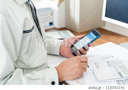 スマホを操作する作業服の男性の手元 118702141