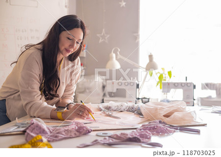 A woman seamstress designs and draws a pattern for underwear on graph paper. A woman seamstress designs and draws a pattern for underwear on graph paper. 118703025